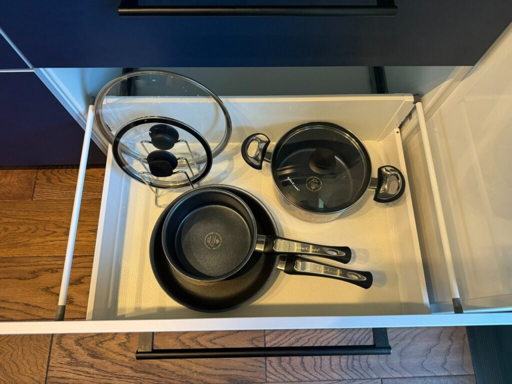 フライパンと鍋、専用のガラス蓋が整然と収納されたキッチン引き出し / Frying pans, pots, and glass lids neatly stored in a kitchen drawer